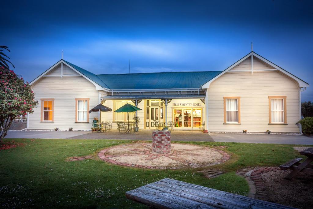 uma grande casa branca com um banco à frente em Karamea Village Hotel em Karamea