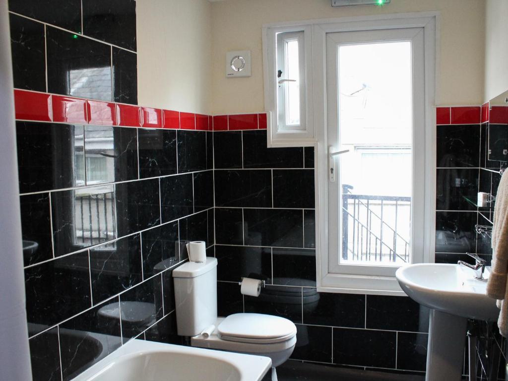 a black tiled bathroom with a toilet and a window at Mary House 46 in Porthcawl