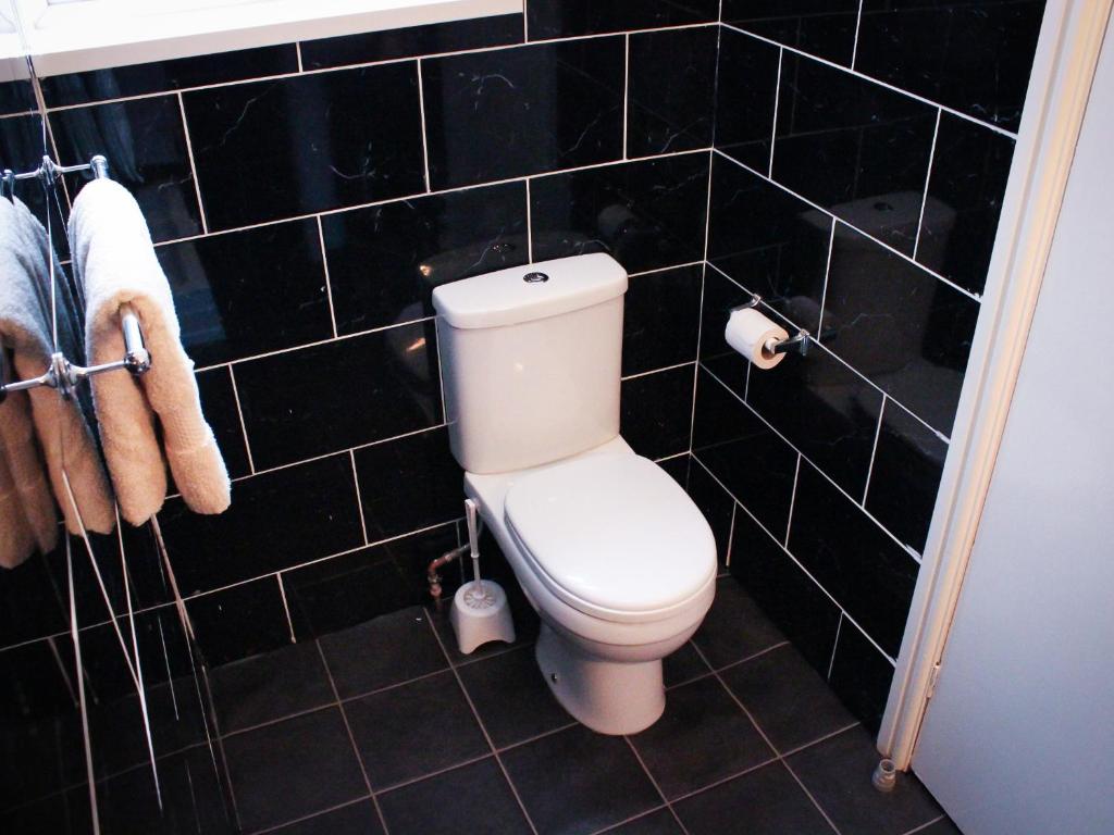 a bathroom with a toilet and black tiled walls at Mary House 46 in Porthcawl
