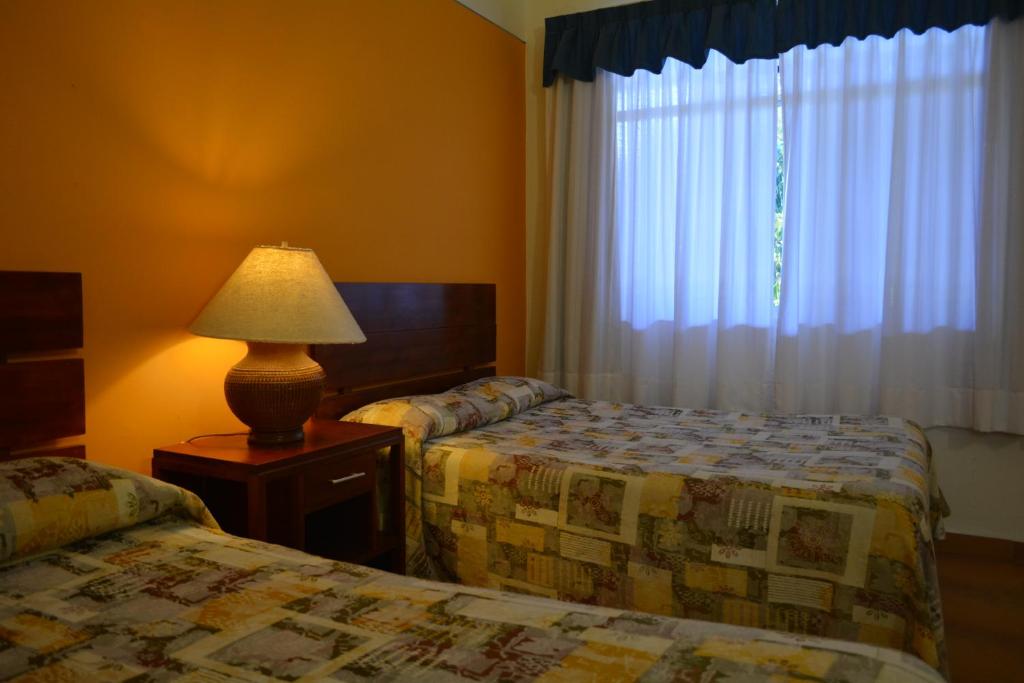 Un dormitorio con dos camas y una lámpara y una ventana. en Lourdes Hotel Campestre, en Santa María del Río