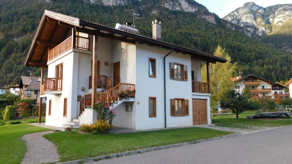a white house with a balcony and mountains in the background at Appartamento Zorzi in Ziano di Fiemme