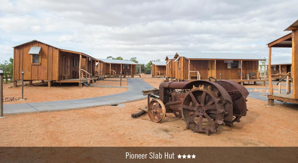a group of wooden huts and a tractor in front of a building at Saltbush Retreat in Longreach