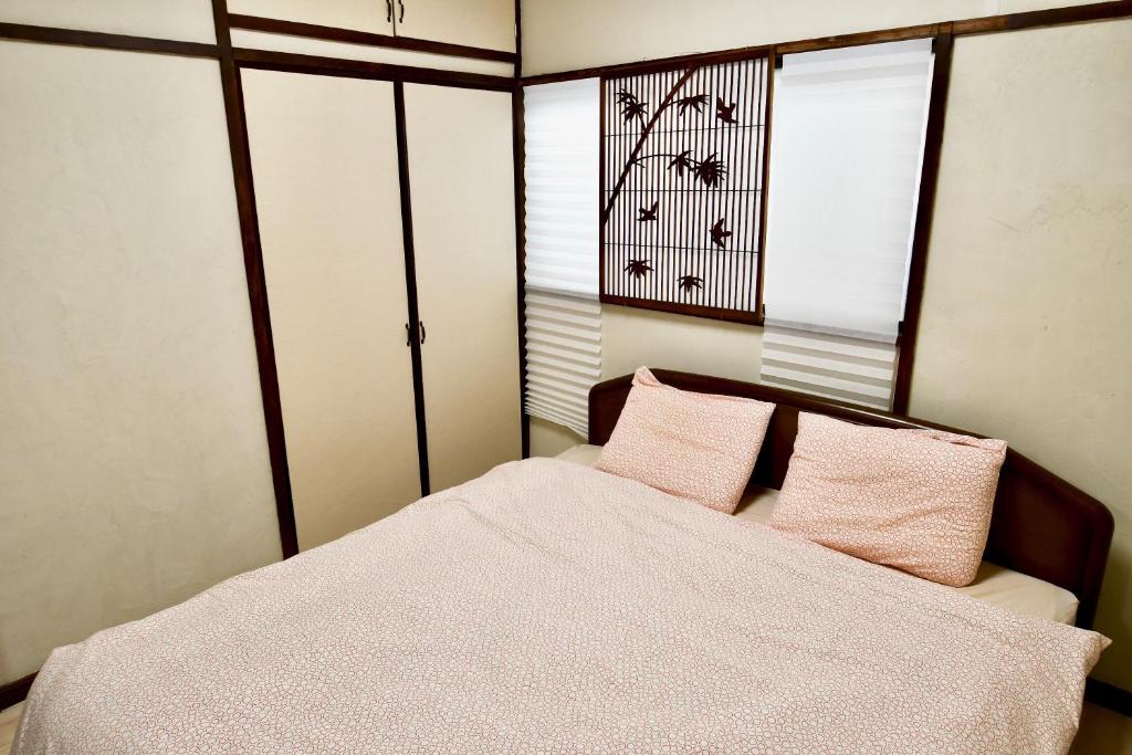 Schlafzimmer mit einem Bett mit rosa Kissen und einem Fenster in der Unterkunft Hostel Hana An in Tokio