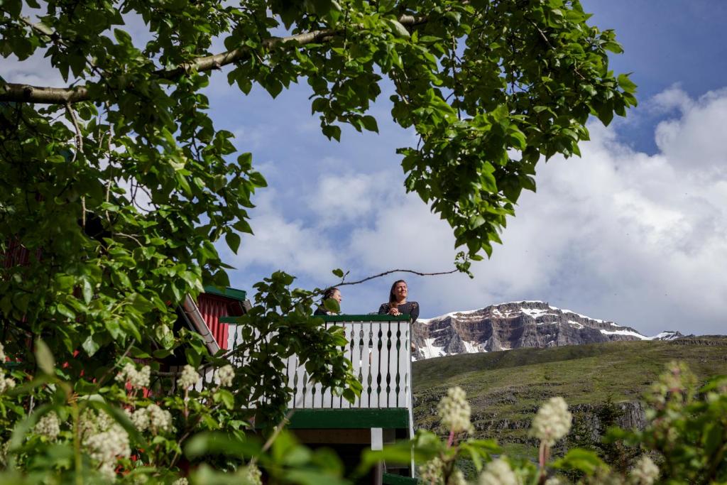 two people sitting on a fence with a mountain in the background at Hafaldan HI hostel, old hospital building in Seyðisfjörður