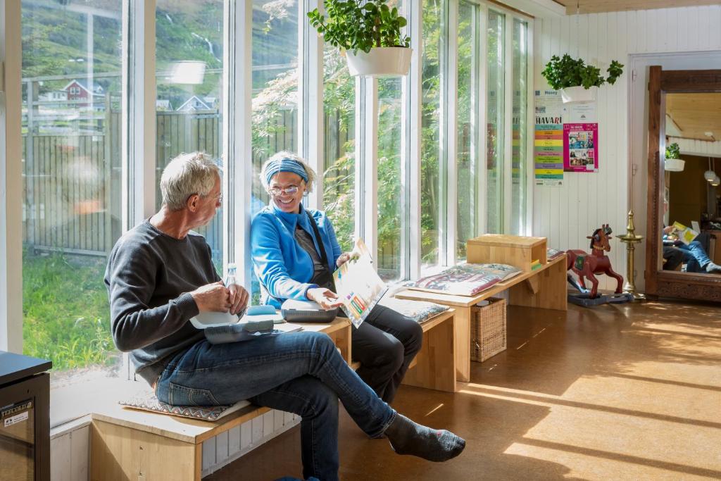 two people sitting on benches in a room with windows at Hafaldan HI hostel, old hospital building in Seyðisfjörður
