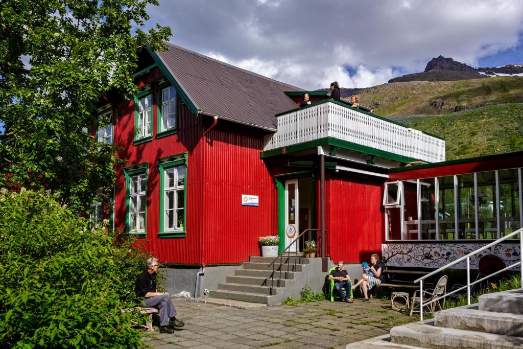 a red building with people sitting outside of it at Hafaldan HI hostel, old hospital building in Seyðisfjörður