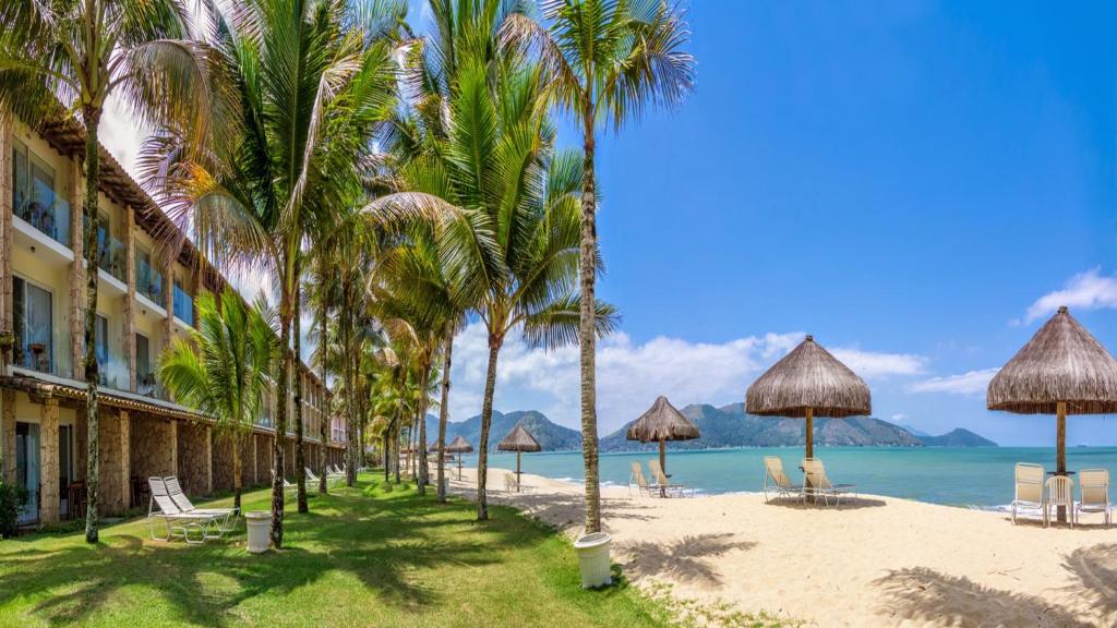 a beach with palm trees and chairs and a hotel at Hotel Portobello Resort & Safari in Mangaratiba