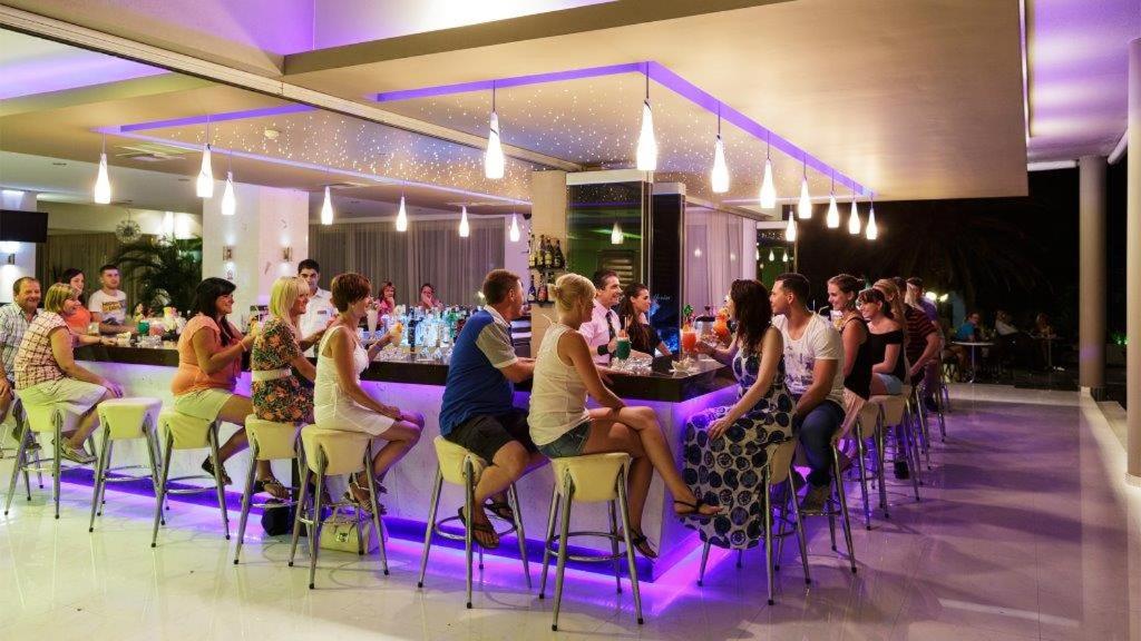 a group of people sitting at a bar in a restaurant at Cathrin Hotel in Faliraki