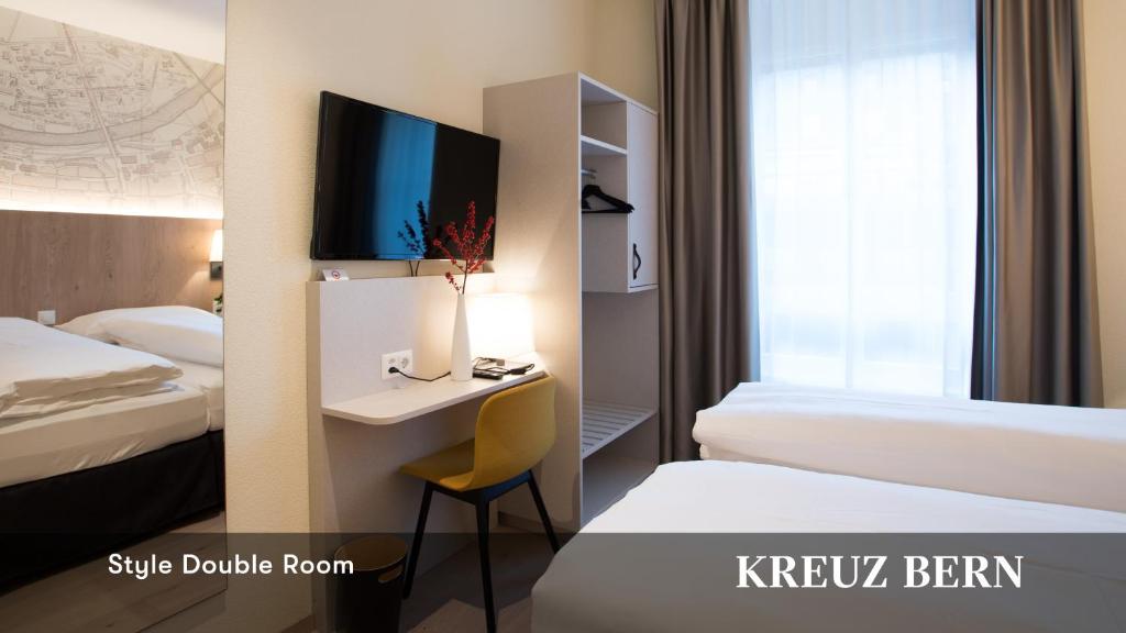 a hotel room with two beds and a desk with a tv at Kreuz Bern Modern City Hotel in Bern