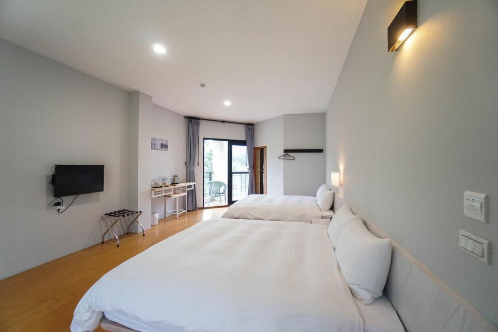 a white bedroom with two beds and a tv at Xi Tou in Sunny Day Inn in Lugu