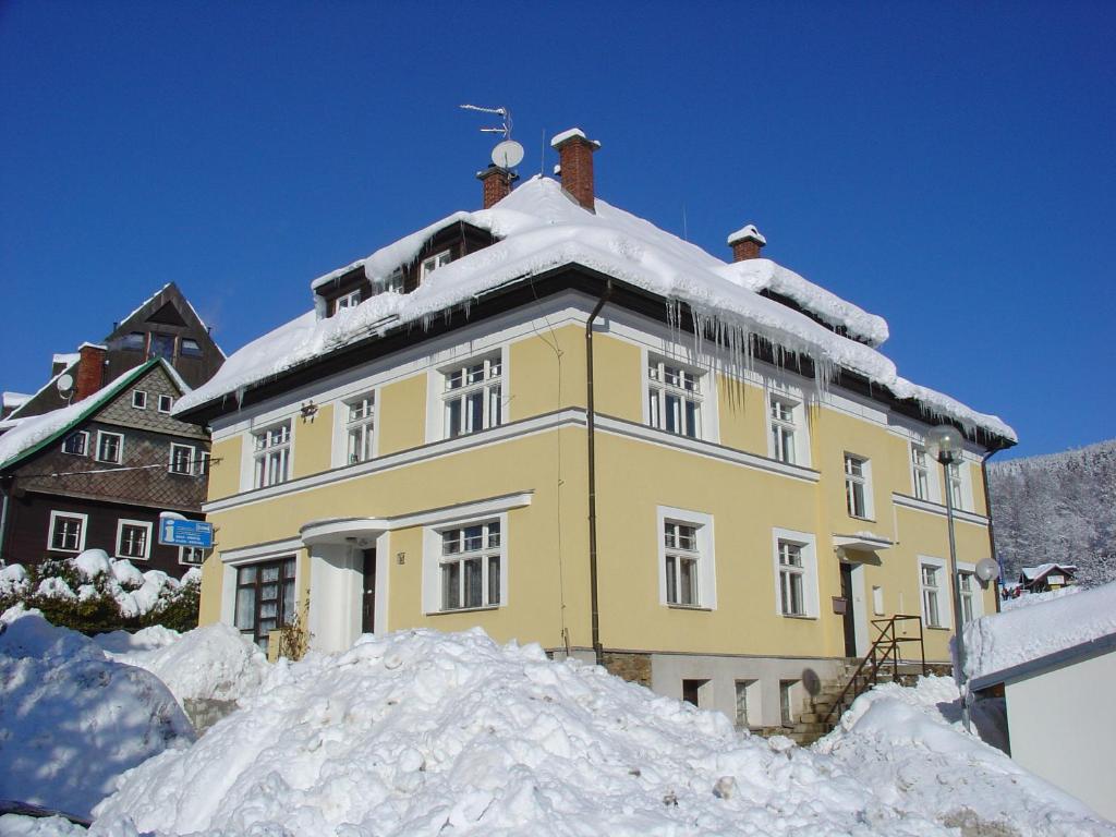 a yellow house with snow on top of it at Penzion Roko in Rokytnice nad Jizerou