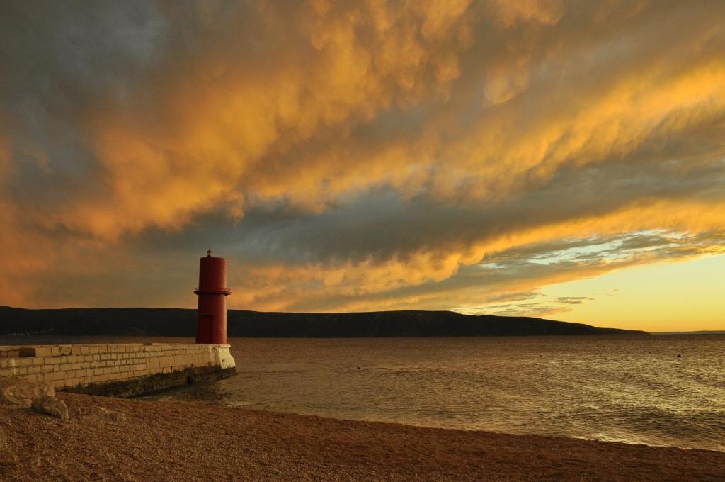 a lighthouse on the shore of the water at sunset at Apartment Mira in Cres