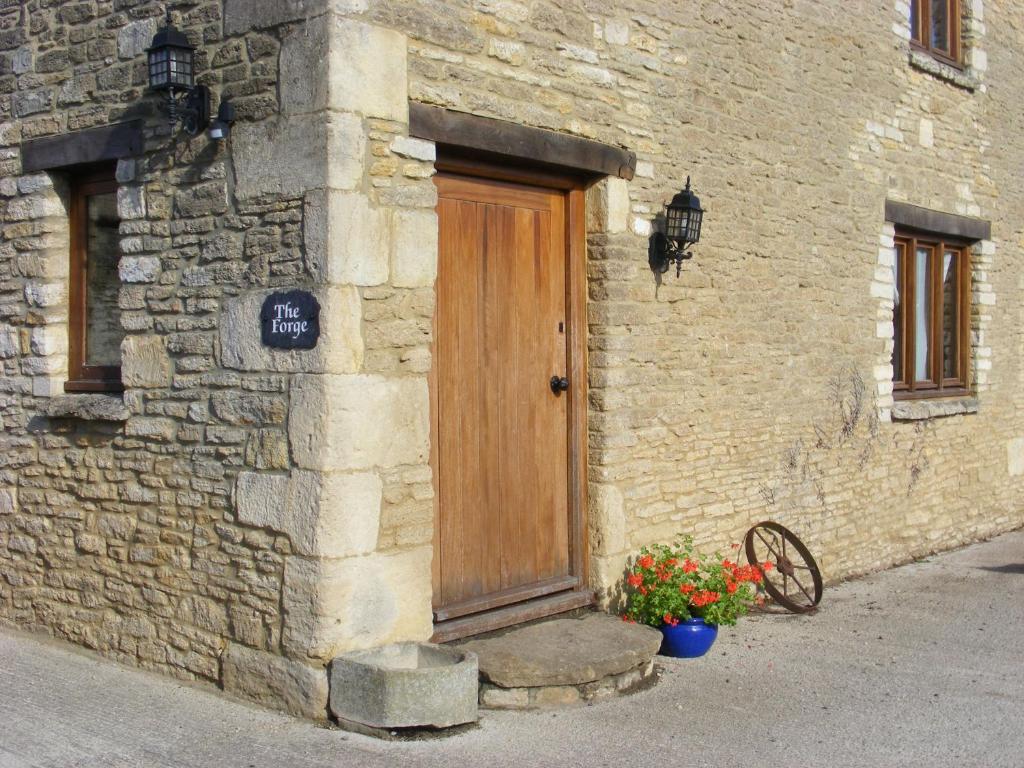 una puerta de madera en el lateral de un edificio de piedra con flores en The Forge, en Corsham