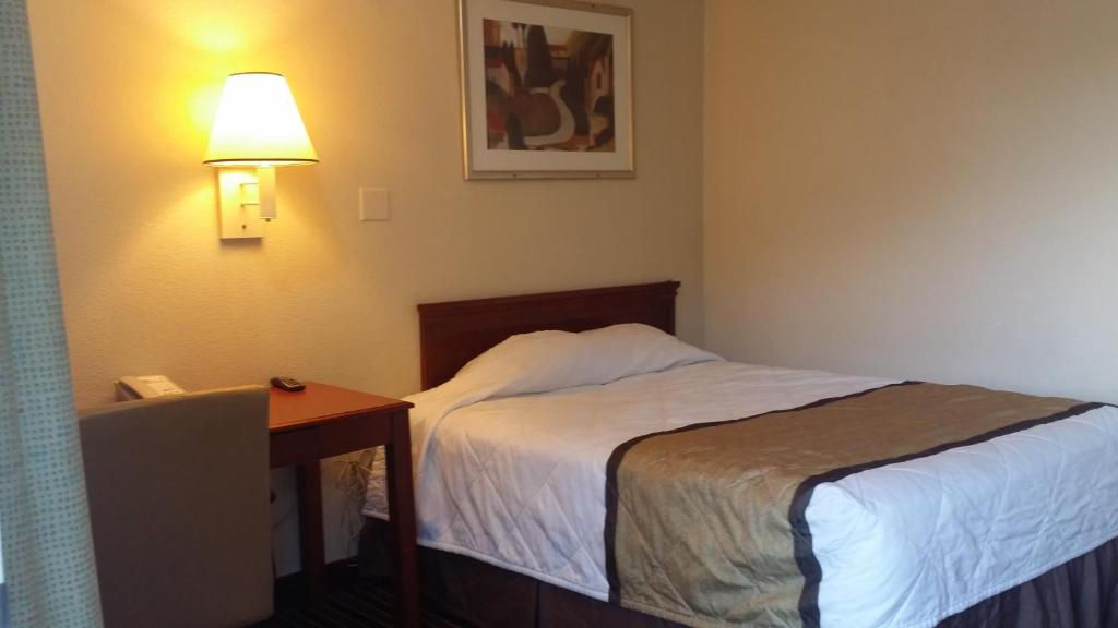 a hotel room with a bed and a desk and a lamp at Carpet Inn in Opelika