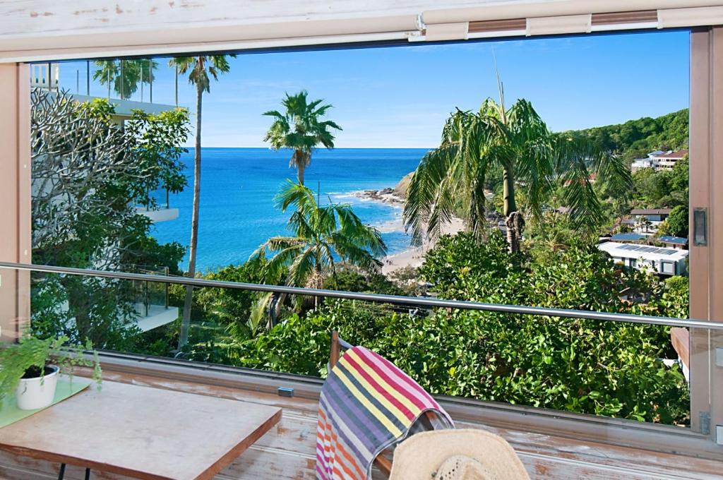 a balcony with a view of the ocean and palm trees at WategosRent in Byron Bay