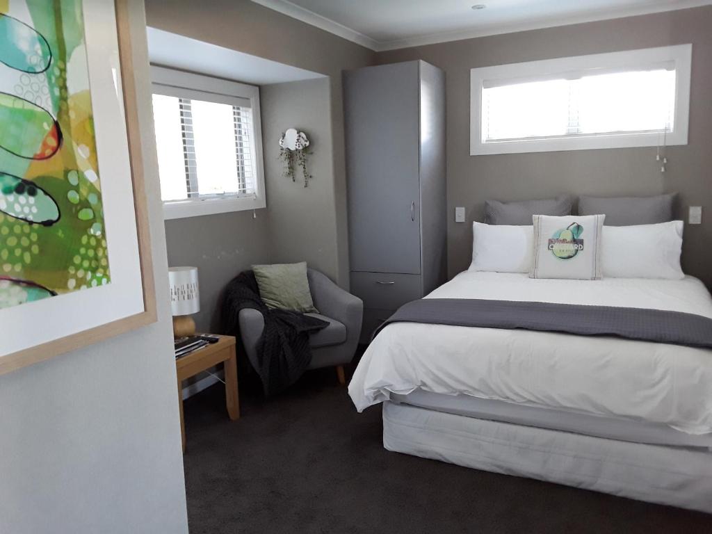 a bedroom with a bed and a chair and two windows at Suite Petite in Taupo