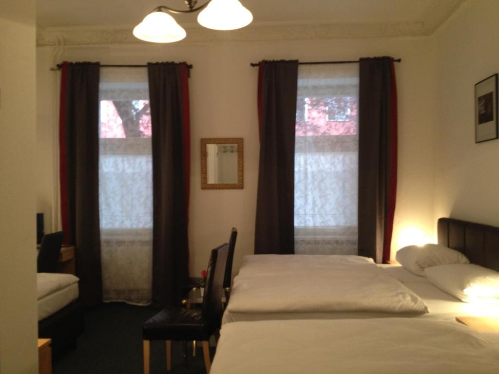 a bedroom with two beds and two windows at Hotel-Pension Dorma in Berlin