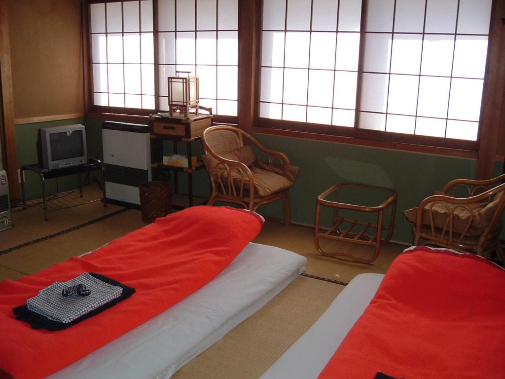 een kamer met 2 bedden, stoelen en ramen bij Onsen Inn 36So in Matsumoto