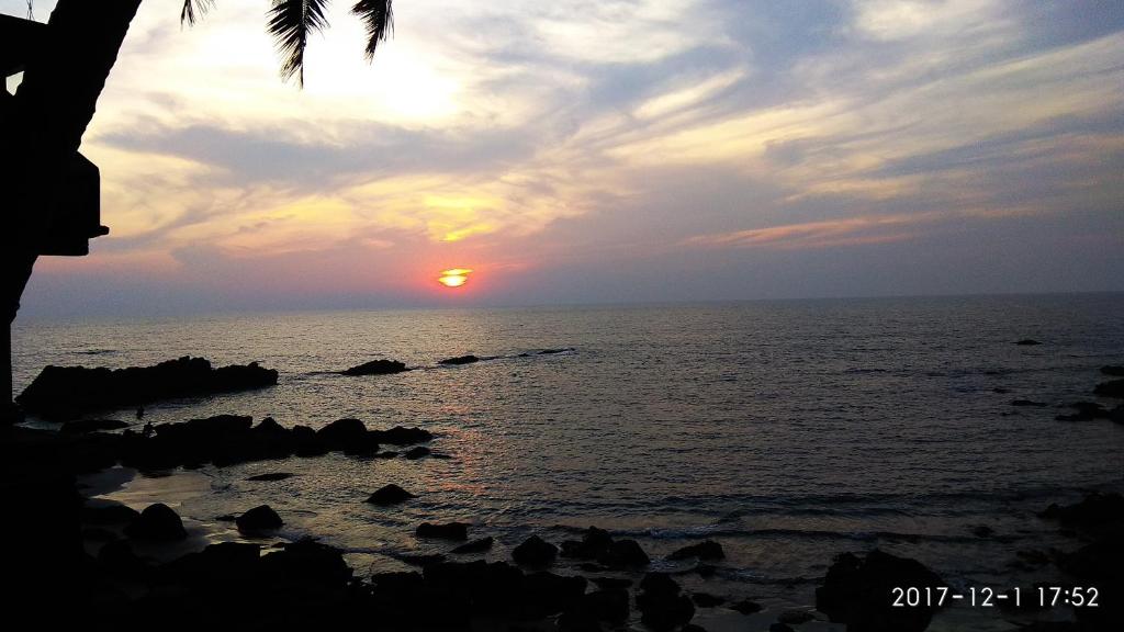 un coucher de soleil sur l'océan avec des rochers dans l'eau dans l'établissement Om Ganesh Guest House Cliffside, à Arambol