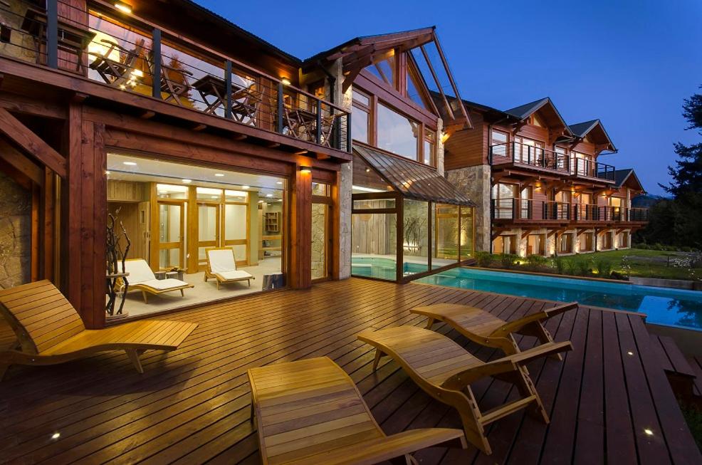Casa con terraza de madera con sillas y piscina en Hostería Huenú en Villa La Angostura