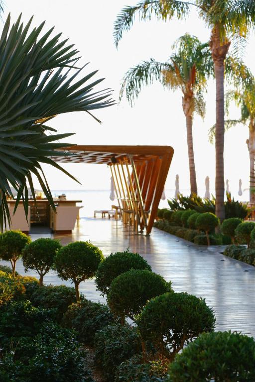 a garden with a wooden table and palm trees at Alimounda Mare Hotel in Karpathos