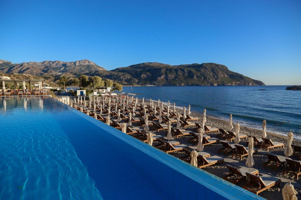 a swimming pool with lounge chairs and the ocean at Alimounda Mare Hotel in Karpathos