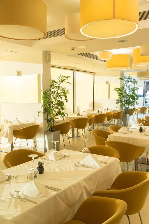 a restaurant with white tables and yellow chairs at Alimounda Mare Hotel in Karpathos