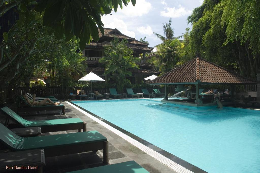 a swimming pool with chairs and a gazebo at Hotel Puri Bambu in Jimbaran