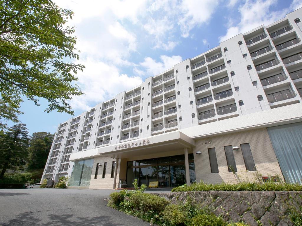 Hotel Kirishima Castle في كيريشيما: مبنى فندق كبير ابيض مع موقف للسيارة