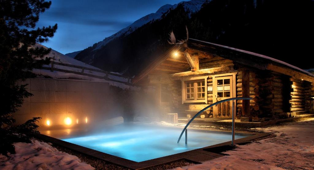 bañera de hidromasaje frente a una cabaña por la noche en Hotel Madlein, en Ischgl