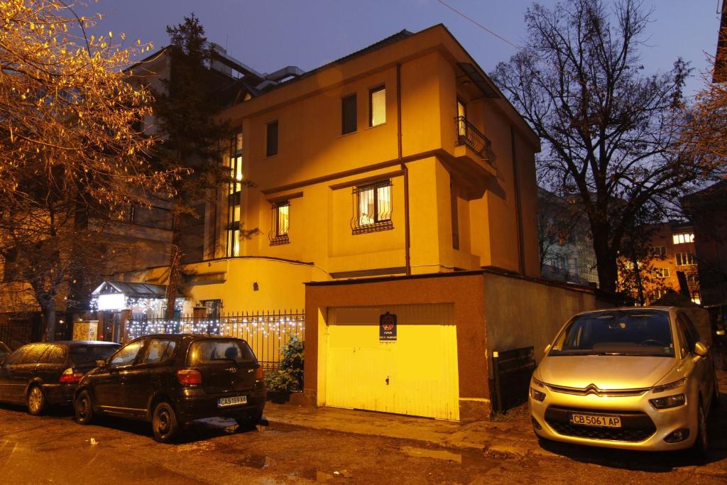 due auto parcheggiate di fronte a un edificio giallo di Guest Rooms Stay Nexus a Sofia