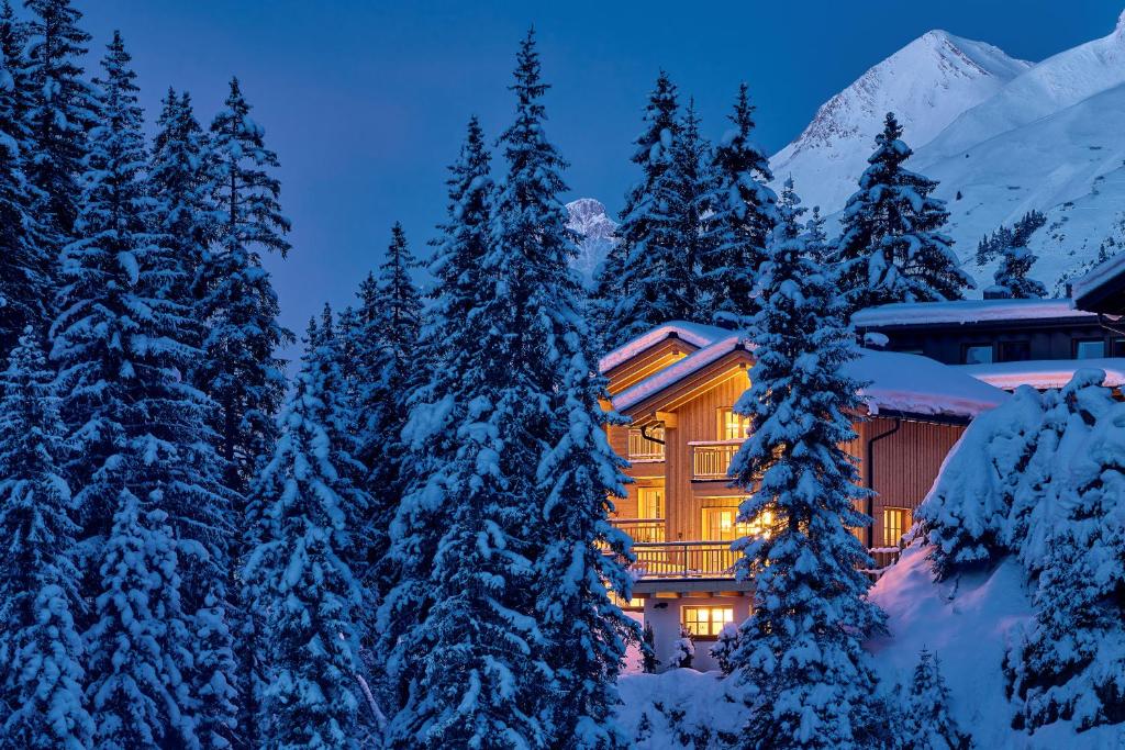 a lodge in the snow at night with snow covered trees at Omesberg-Hütt'n in Lech am Arlberg