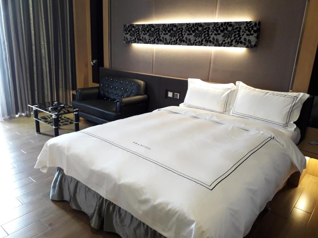 um quarto com uma grande cama branca e uma cadeira em Yunlin Commerce Ryokan em Tuku