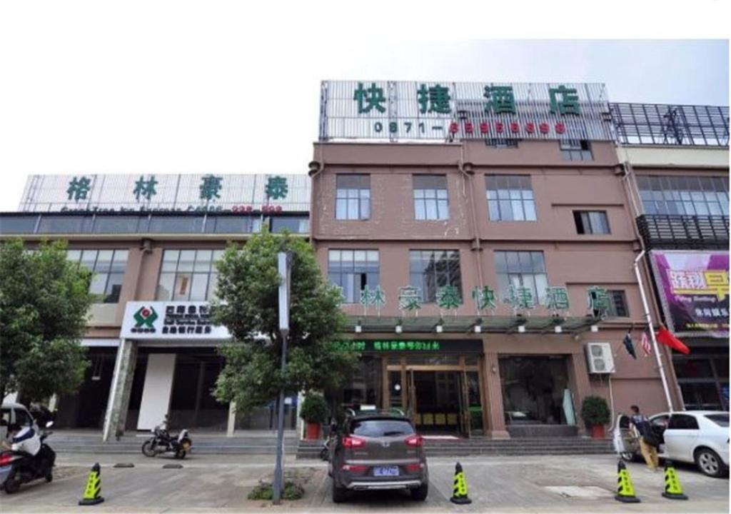 GreenTree Inn Yunnan Kunming Chenggong University City Shilin Street Express Hotel في كونمينغ: مبنى على شارع فيه سيارات تقف امامه