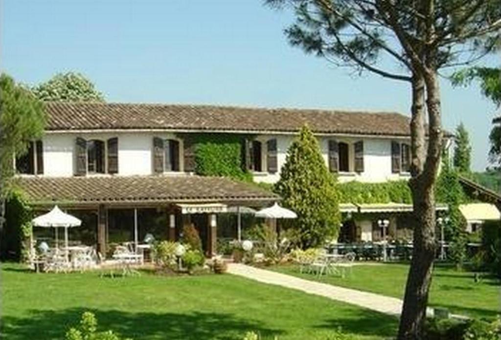 une grande maison avec une cour verdoyante dotée de tables et de parasols dans l'établissement Le Ratelier, à Montaigut-sur-Save