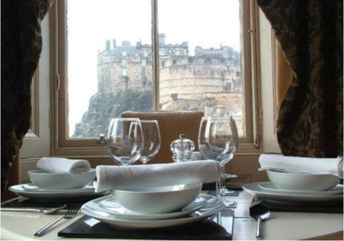 a table with plates and wine glasses and a window at The Castle Esplanade Residence in Edinburgh