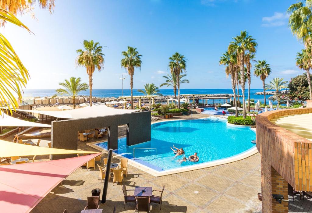 a pool with palm trees and the ocean in the background at Calheta Beach - All-inclusive - Savoy Signature in Calheta