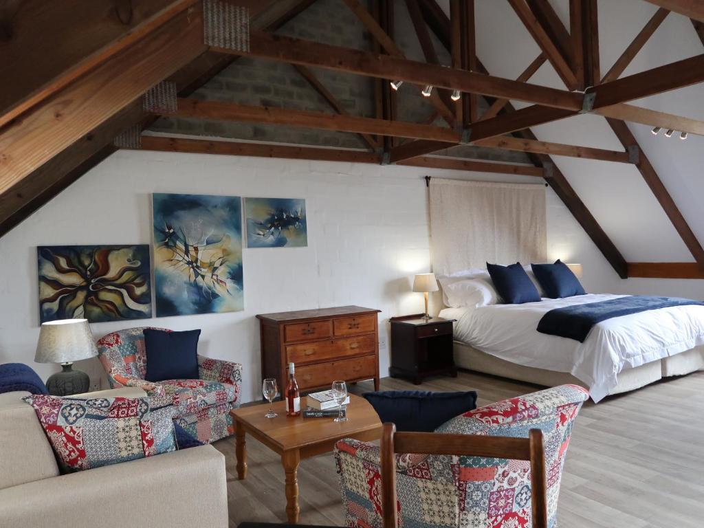 a bedroom with a bed and a couch and chairs at Hemel en Aarde Village Accommodation in Hermanus