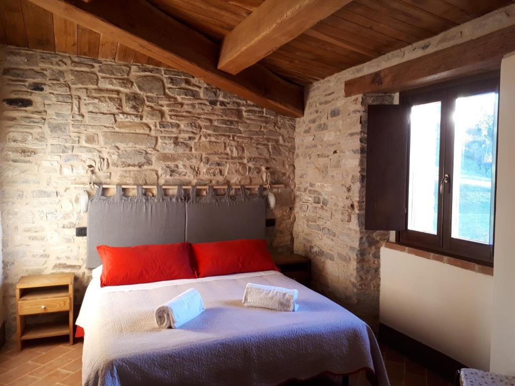 1 dormitorio con 1 cama con almohadas rojas y pared de piedra en Il Gelso Room&breakfast, en Pennabilli