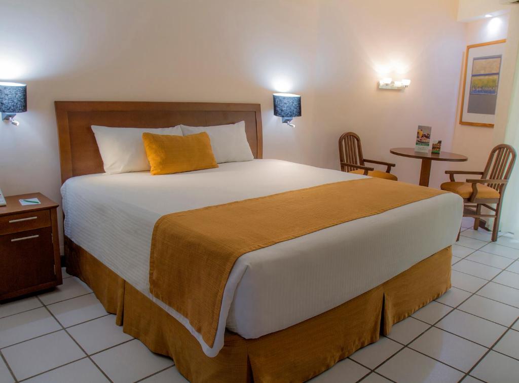 Hotel Viva Villahermosa في فيلاهيرموسا: غرفة نوم بسرير كبير وطاولة وكراسي