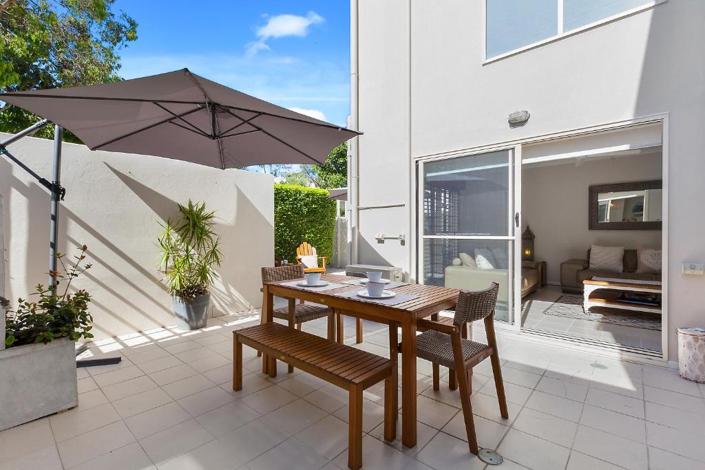 eine Terrasse mit einem Holztisch, Stühlen und einem Sonnenschirm in der Unterkunft The Courtyards on Hill St in Sunshine Beach