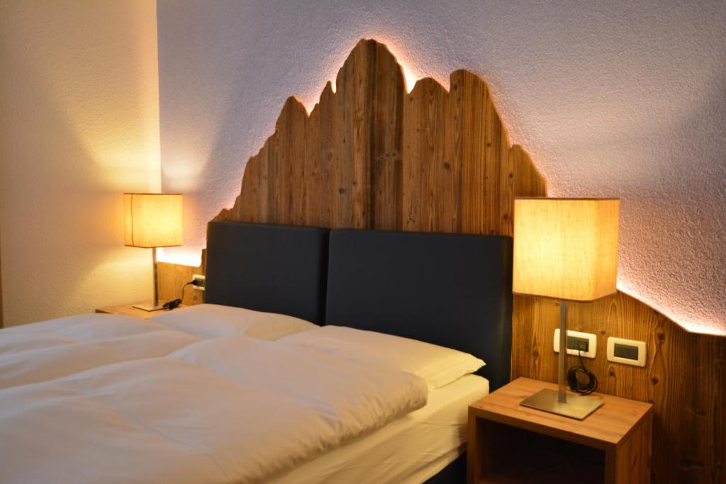 a bedroom with a large white bed with two lamps at Hotel Garnì Nès Crépes in Pozza di Fassa