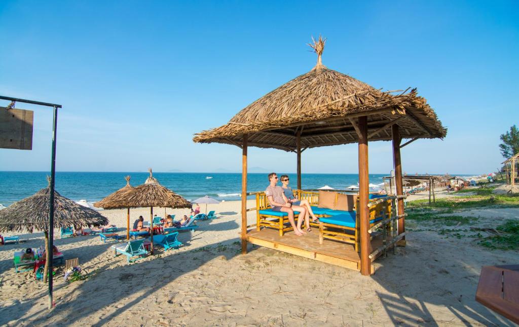 um grupo de pessoas sentadas em cadeiras sob um guarda-sol na praia em Local Beach Homestay em Hoi An