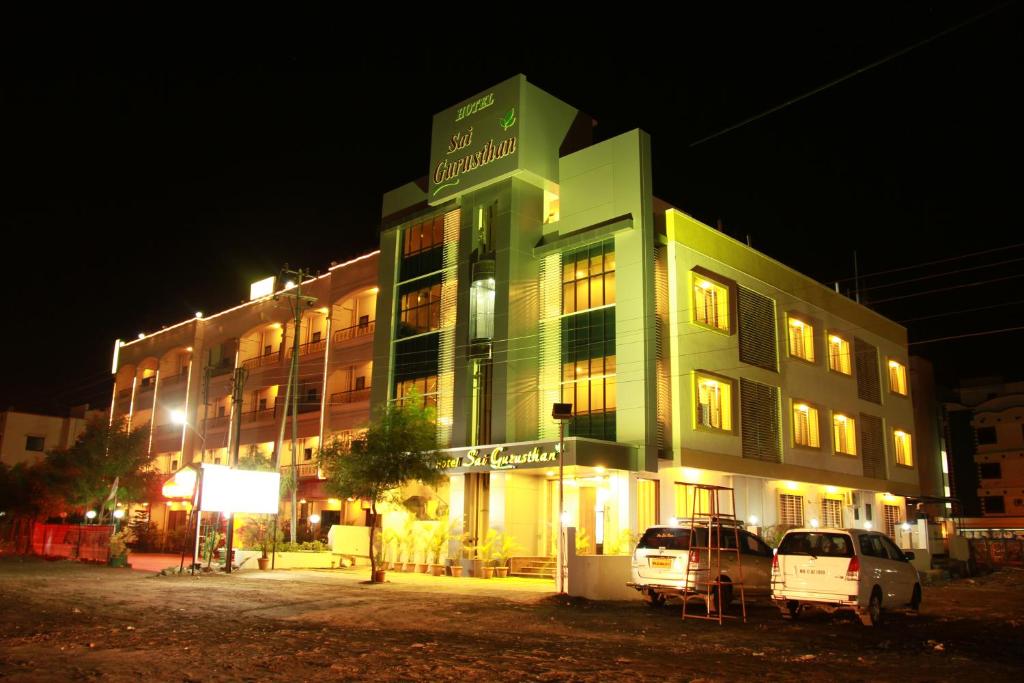 a green building with two cars parked in front of it at Hotel Sai Gurusthan in Shirdi