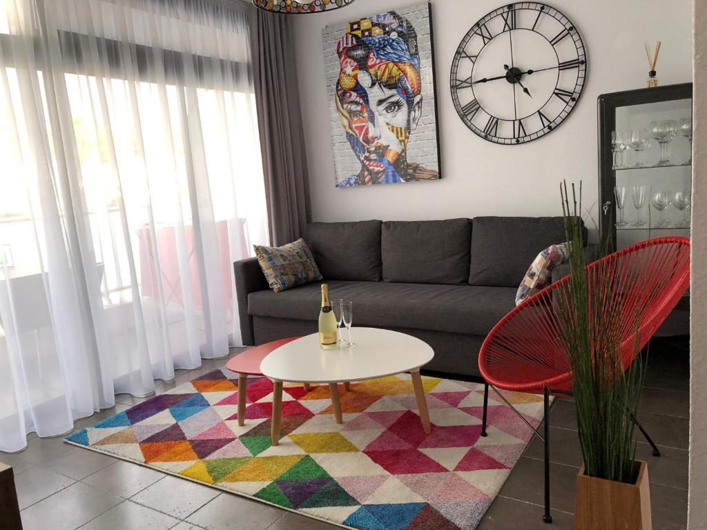 sala de estar con sofá, mesa y reloj en Yumbo Apartments, en Maspalomas
