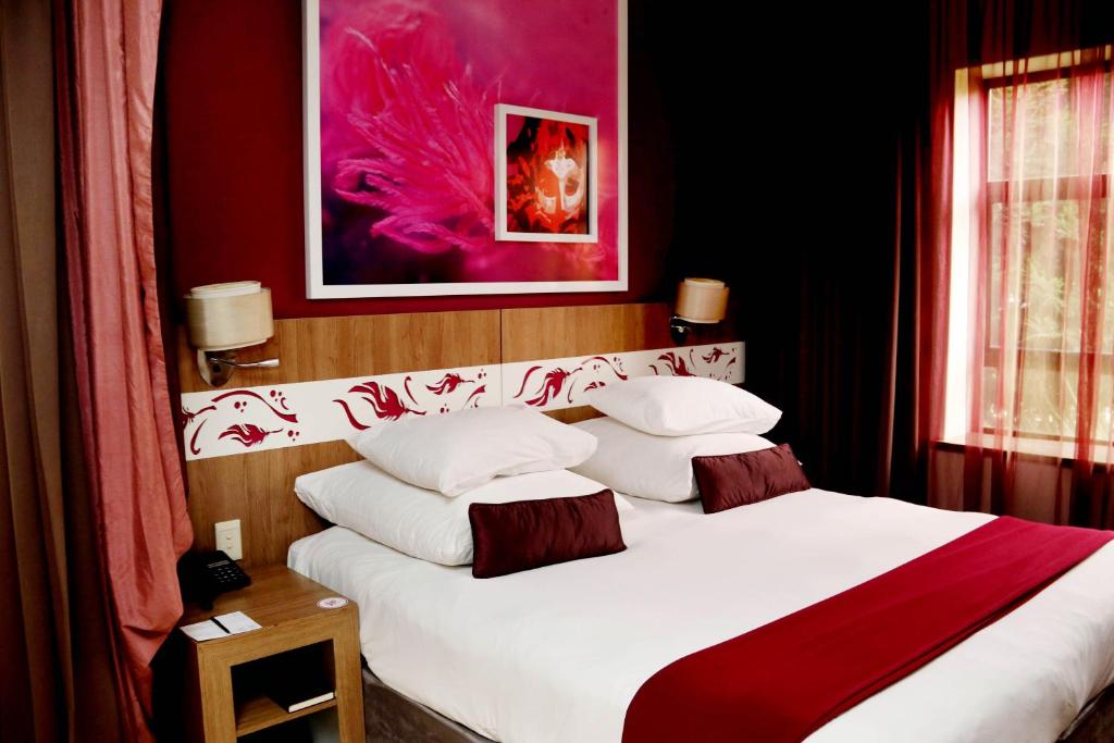 a bedroom with a large white bed with red accents at Peermont Metcourt at Rio, Klerksdorp in Klerksdorp