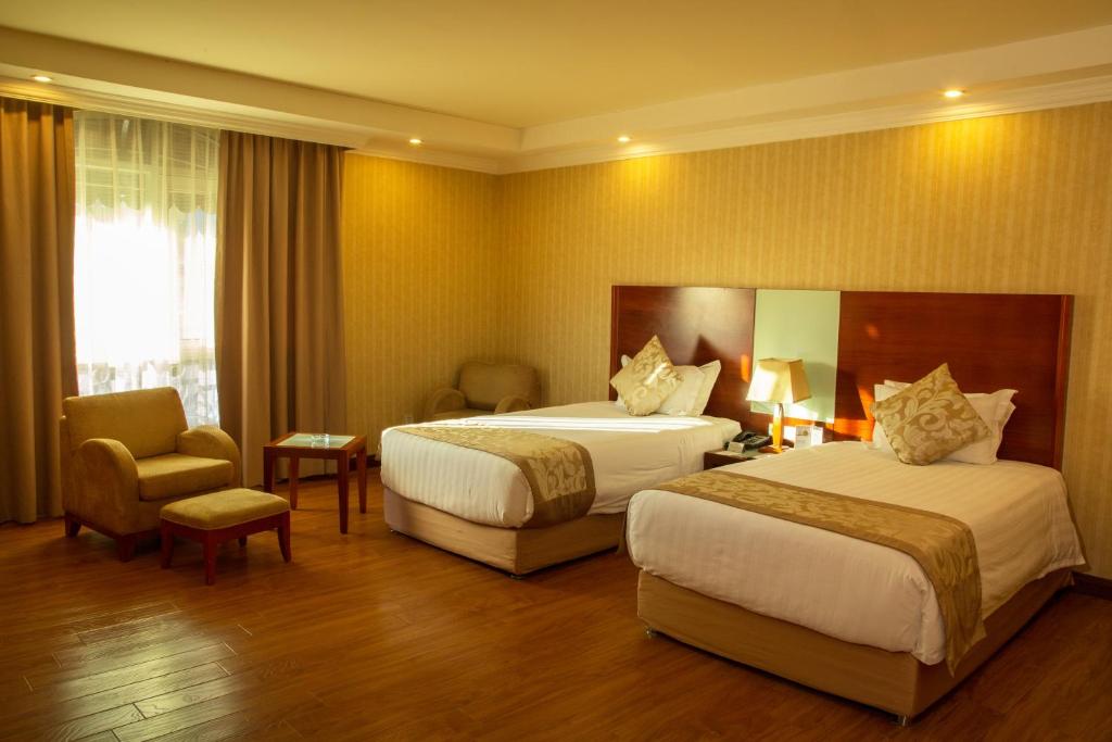 a hotel room with two beds and a chair at Jupiter International Hotel - Bole in Addis Ababa