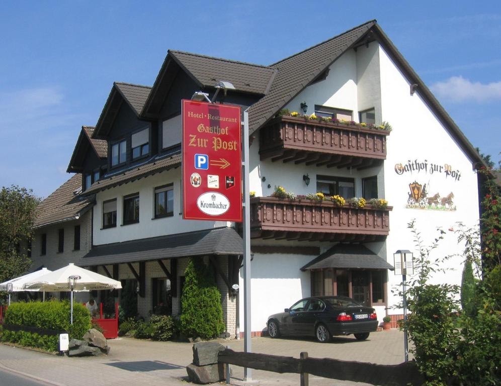 um grande edifício branco com um sinal vermelho em frente em Gasthof zur Post Hotel - Restaurant em Breckerfeld