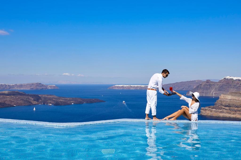 un hombre y una mujer de pie en la parte superior de una piscina en Suites of the Gods Cave Spa Hotel, en Megalokori
