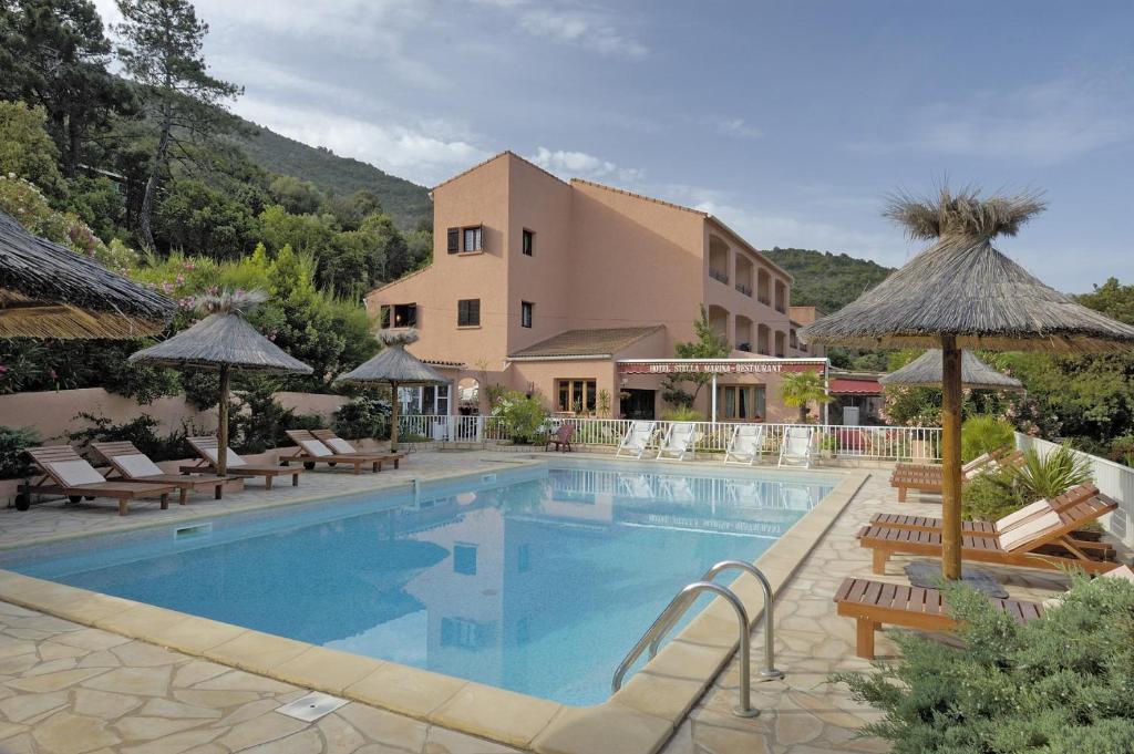 a swimming pool with chairs and umbrellas next to a building at Hotel Stella Marina in Serriera